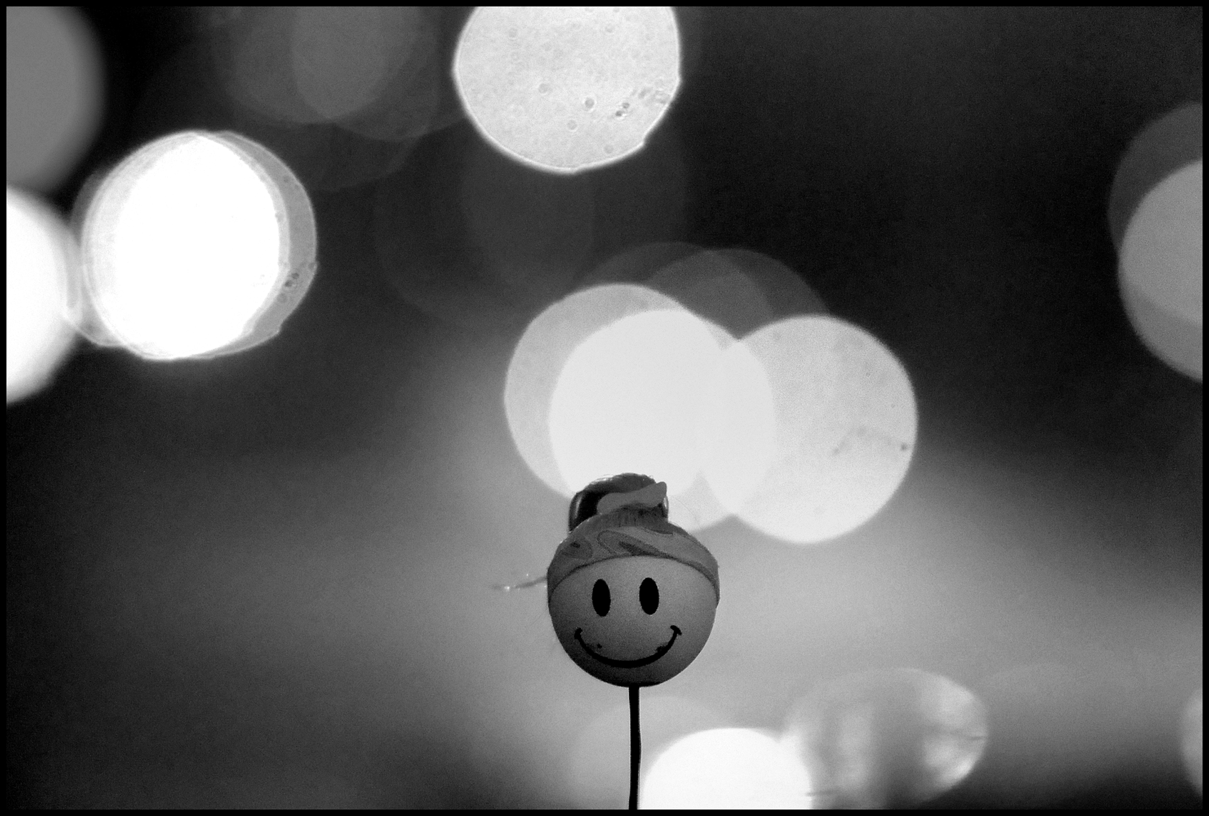 A smiley face on a ping-pong ball on a stick with blurry spotlights in the background.