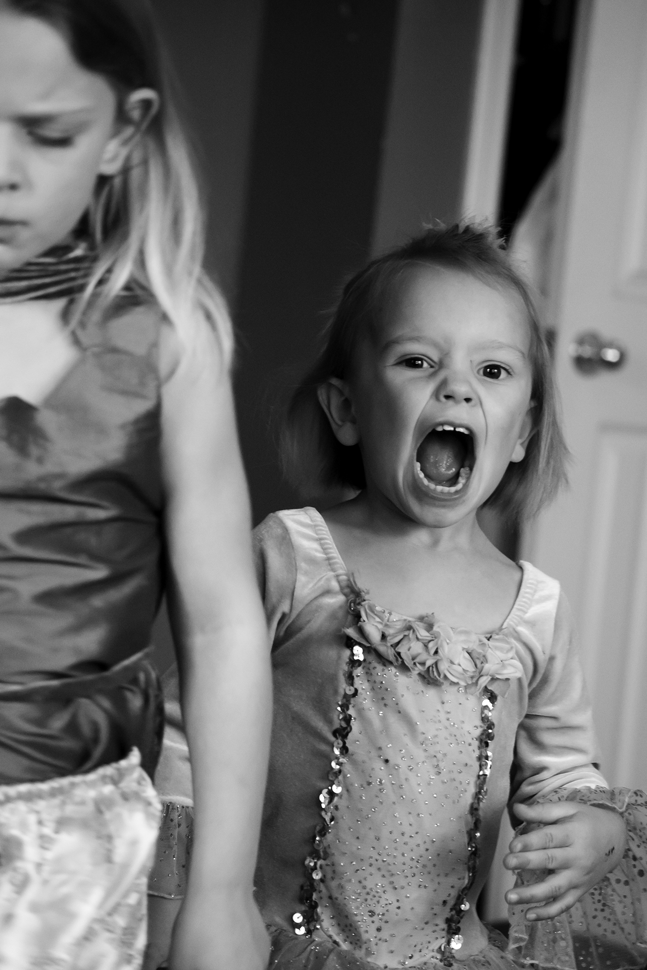 A young girl screaming near an older girl who has her eyes closed and looks frustrated.