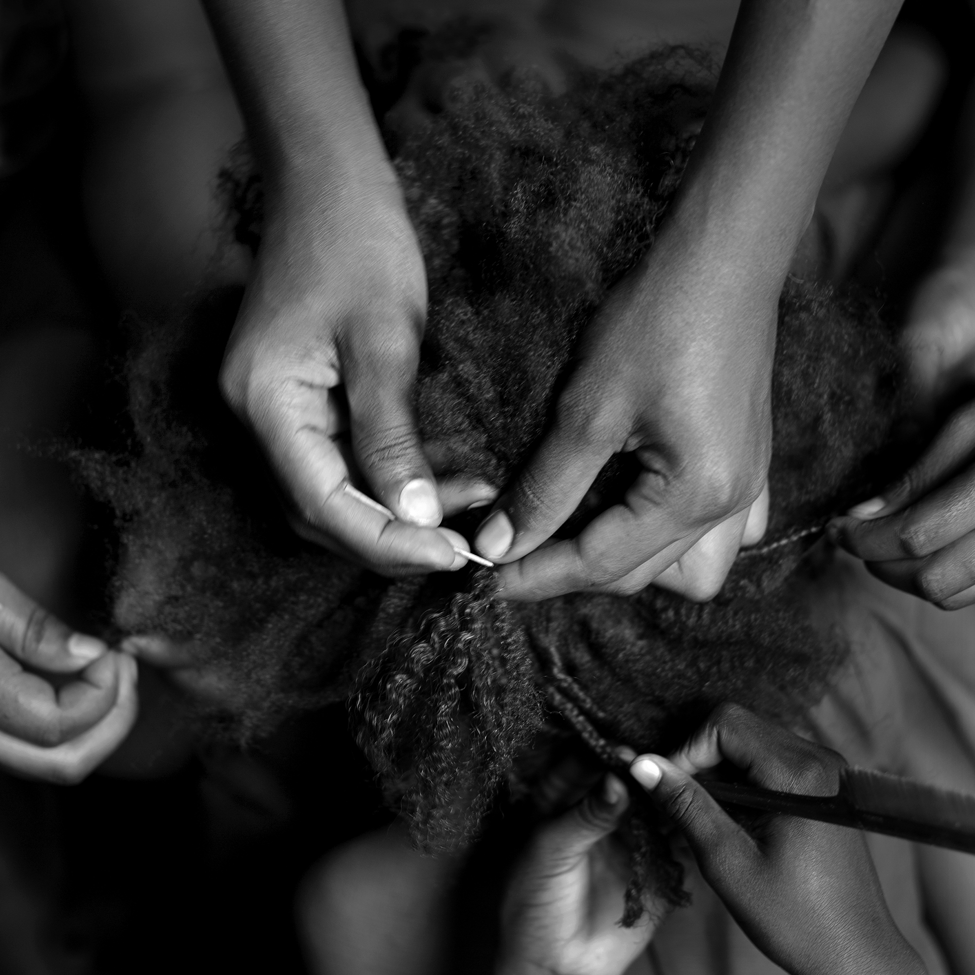 A top-down view of several pairs of hands braiding African American hair.