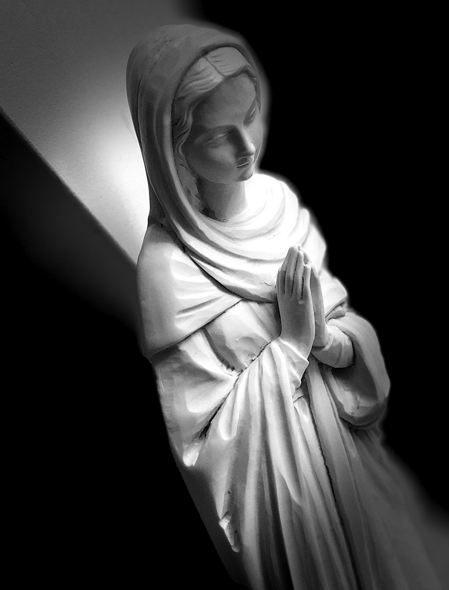 A statue of a woman in a loose gown with a headscarf whose hands are pressed together in prayer.