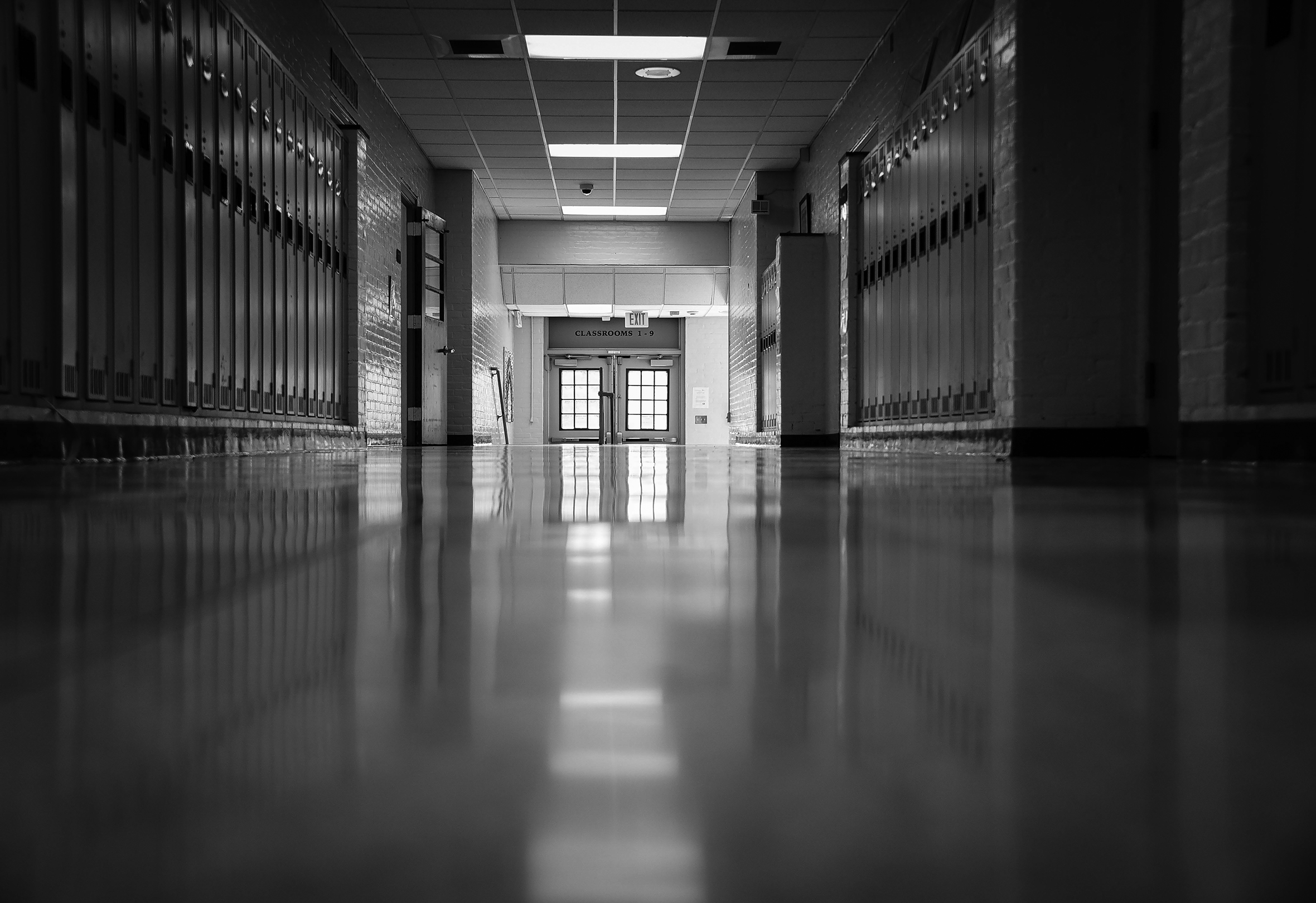 An empty school hallway lined with lockers and double-doors at the end of the hall.