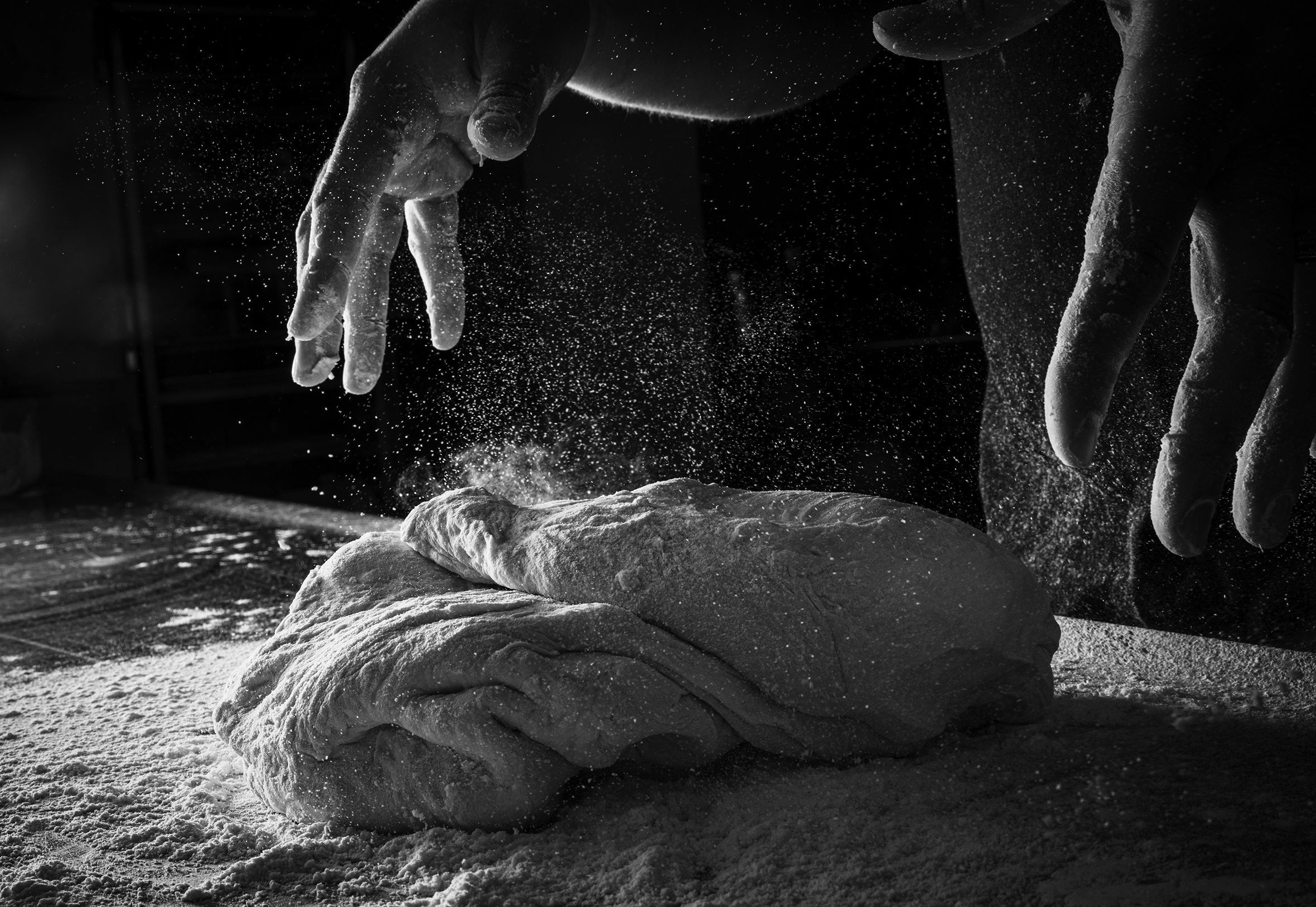 A close-up of a person's hands throwing dough onto a floured table.