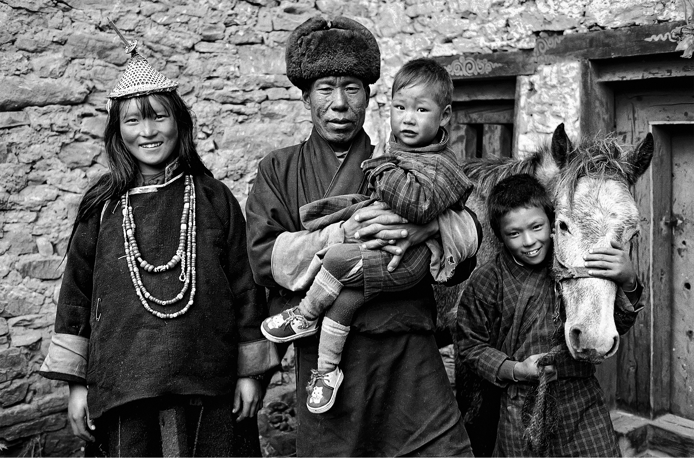 A Bhutanese family and a horse. The wife and husband are wearing traditional clothing. The husband is holding one of their young children. Their other child, an older boy, is standing beside his father and has an arm wrapped around the horse’s muzzle.