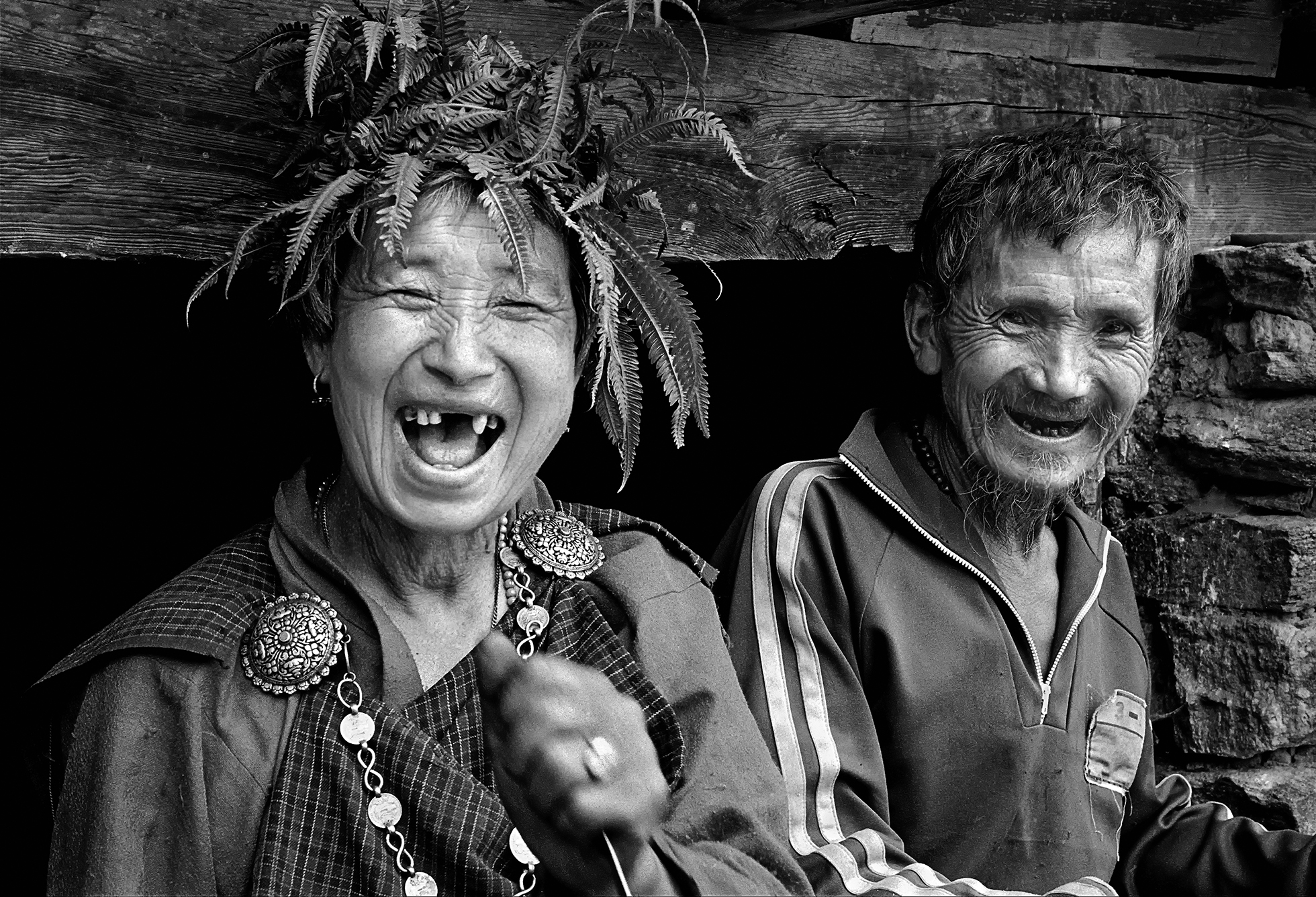 An old Bhutanese couple. The woman is in traditional clothing and is laughing, showing her missing front teeth. Next to her, her husband is also laughing but he’s wearing more modern clothing.