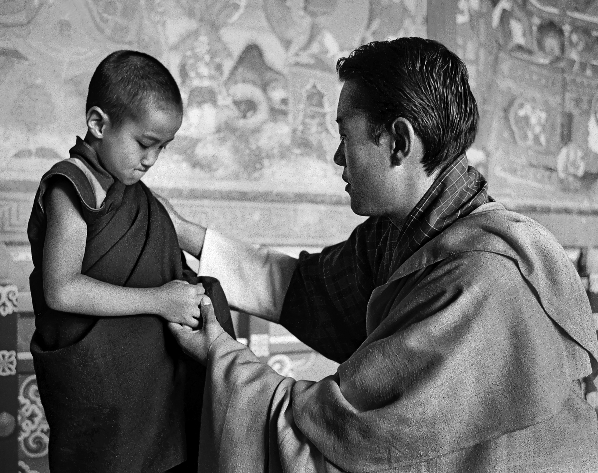 The Crown Prince of Bhutan (at the time of the photo) kneels down and places his hand on a young monk’s shoulder as he speaks to him. The young monk looks disappointed in something.