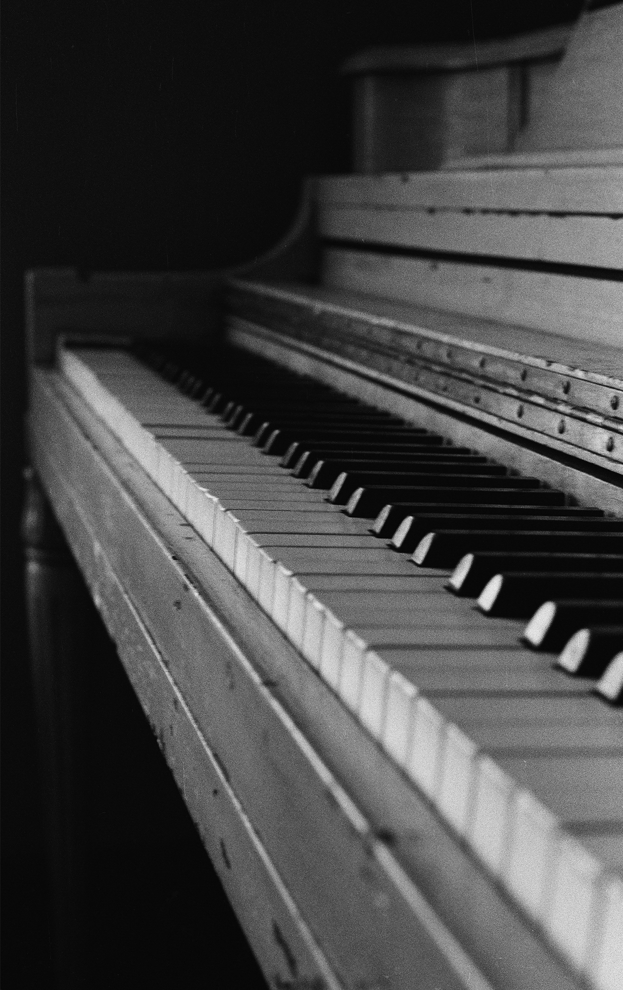 A close-up of the keys on an upright piano. The piano has some chips and dents in its wood.