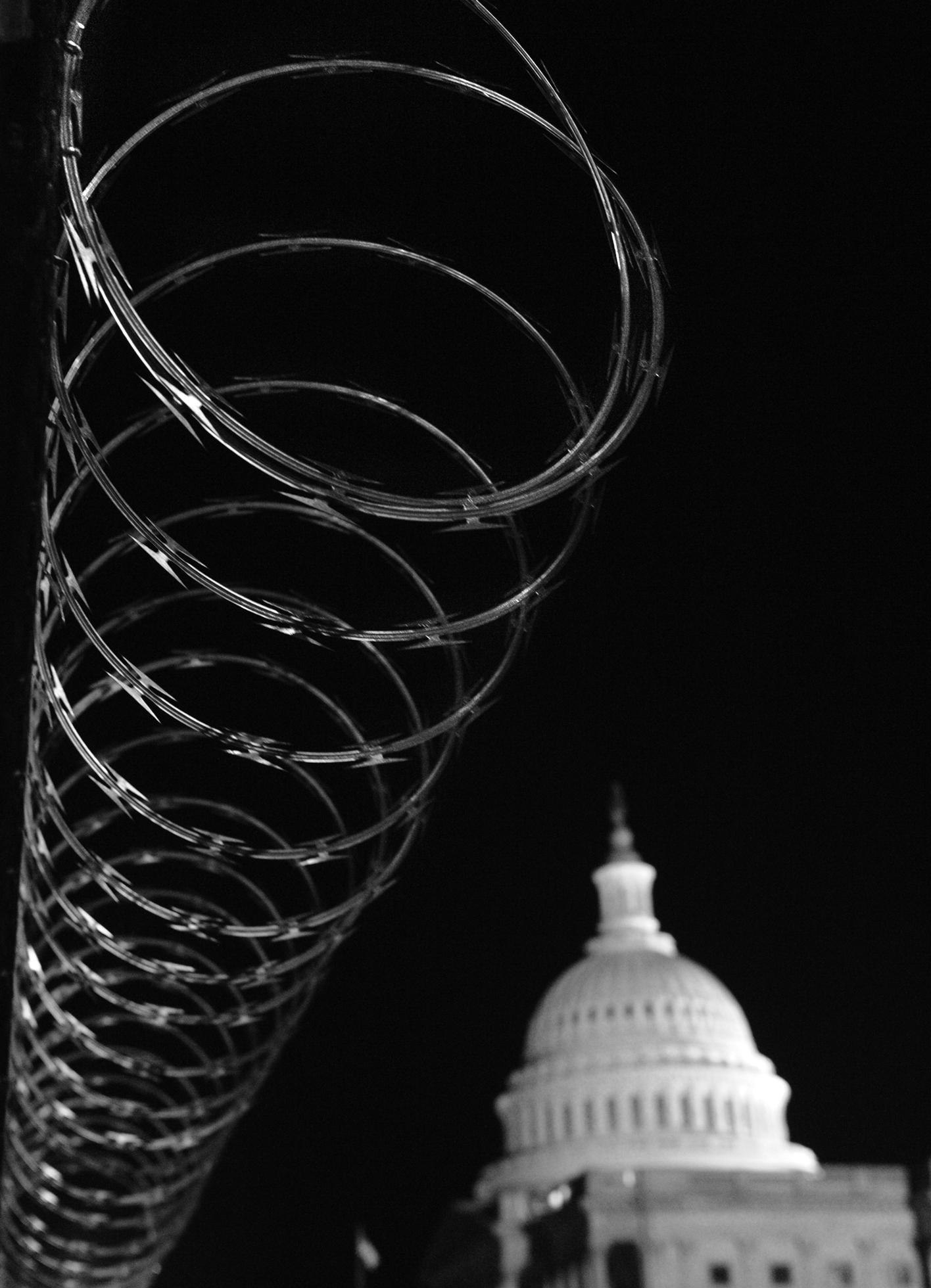 A close-up of razor wire with the Capitol’s dome off in the distance and slightly blurred.