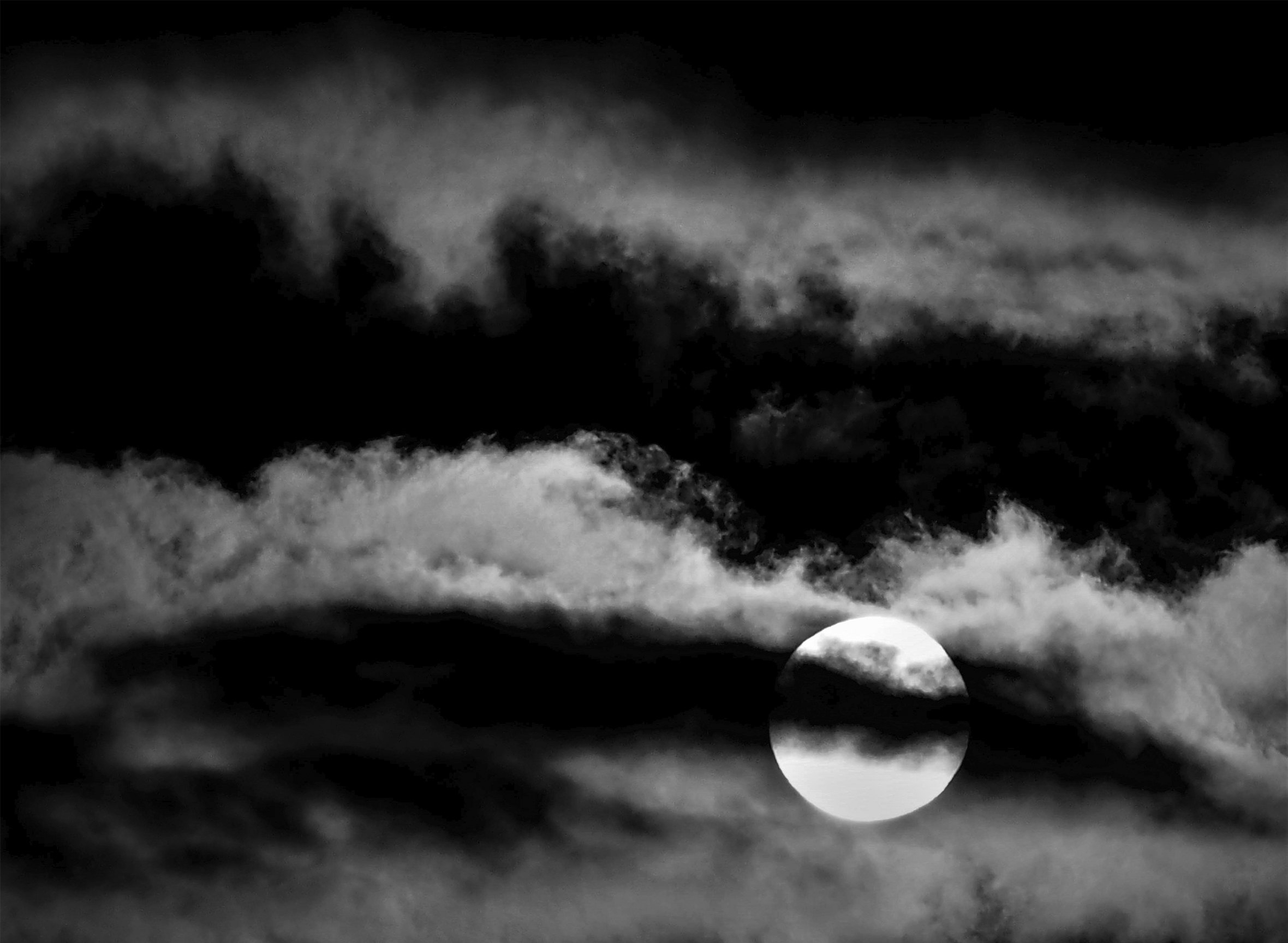 A night sky with strips of clouds that span the entire image in layers. A dark cloud that cuts across the middle of the full moon.