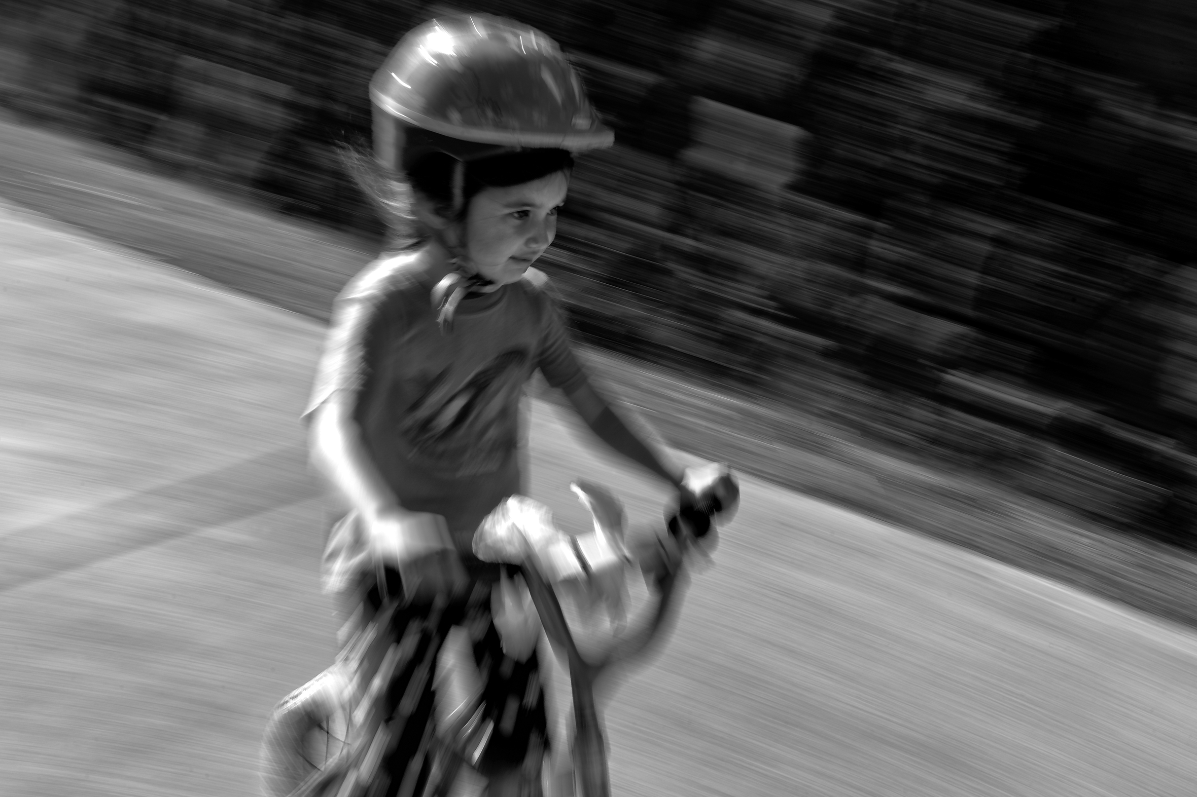 A young girl wearing a helmet, who looks as though she is concentrating, is riding a bike. Her face is clear, but the rest of the photo is motion blurred.