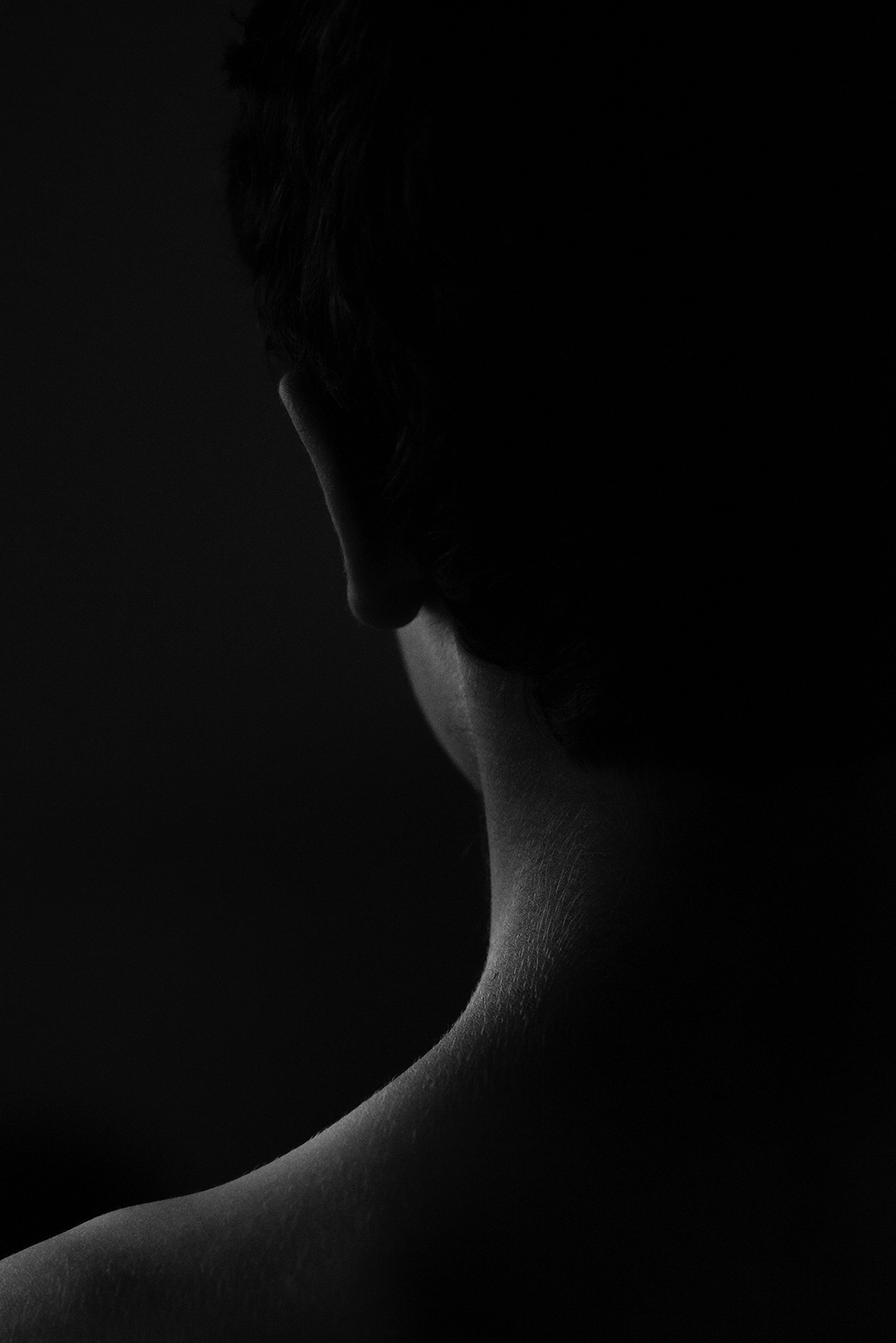 The back view of the darkened silhouette of the left side of a man from his bare shoulder up.