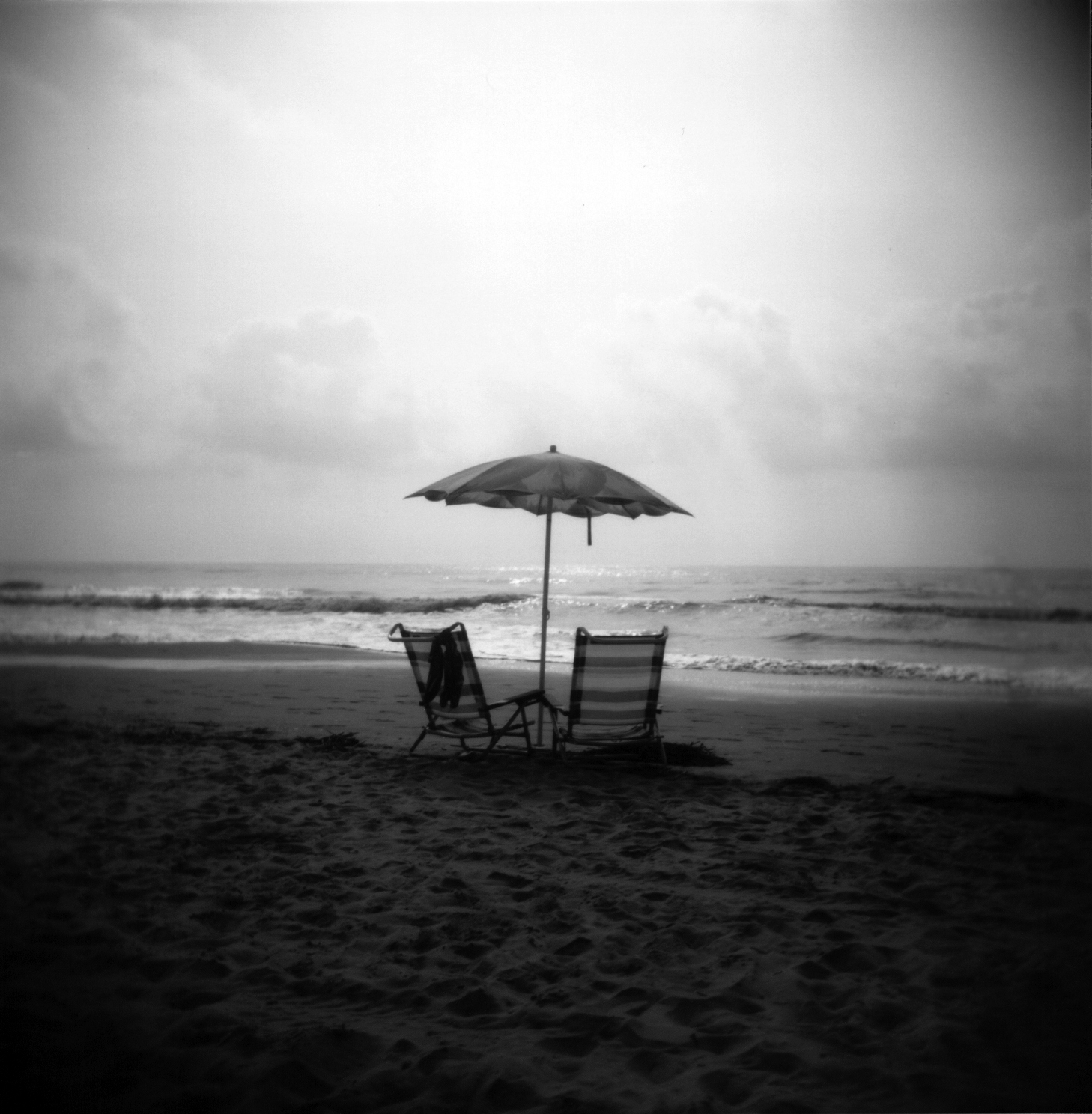 Two striped beach chairs and an umbrella on a sandy beach.