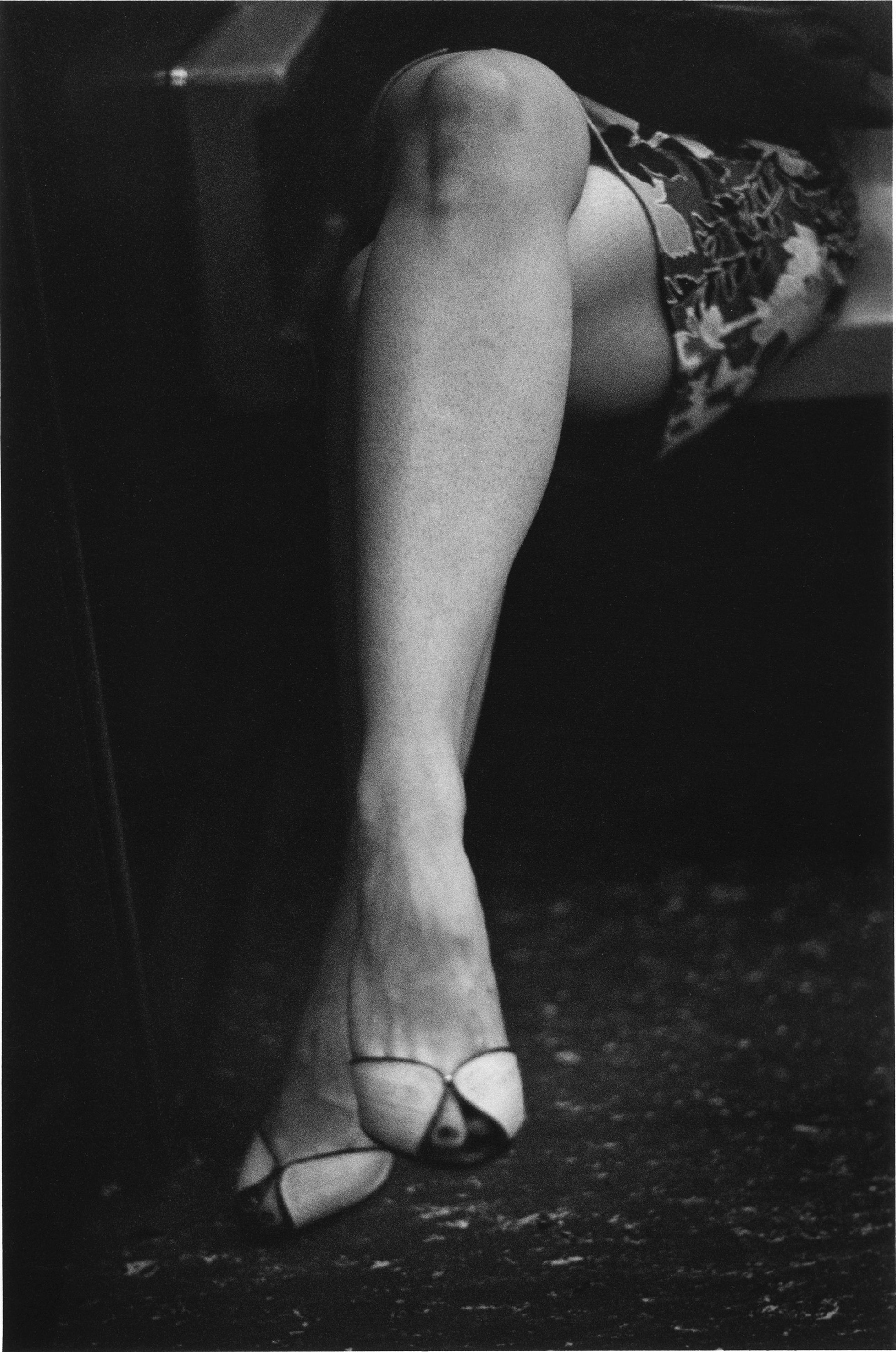 A close-up of a woman’s crossed, bare legs. A leaf-print skirt is visible and she is wearing peep-toe shoes.