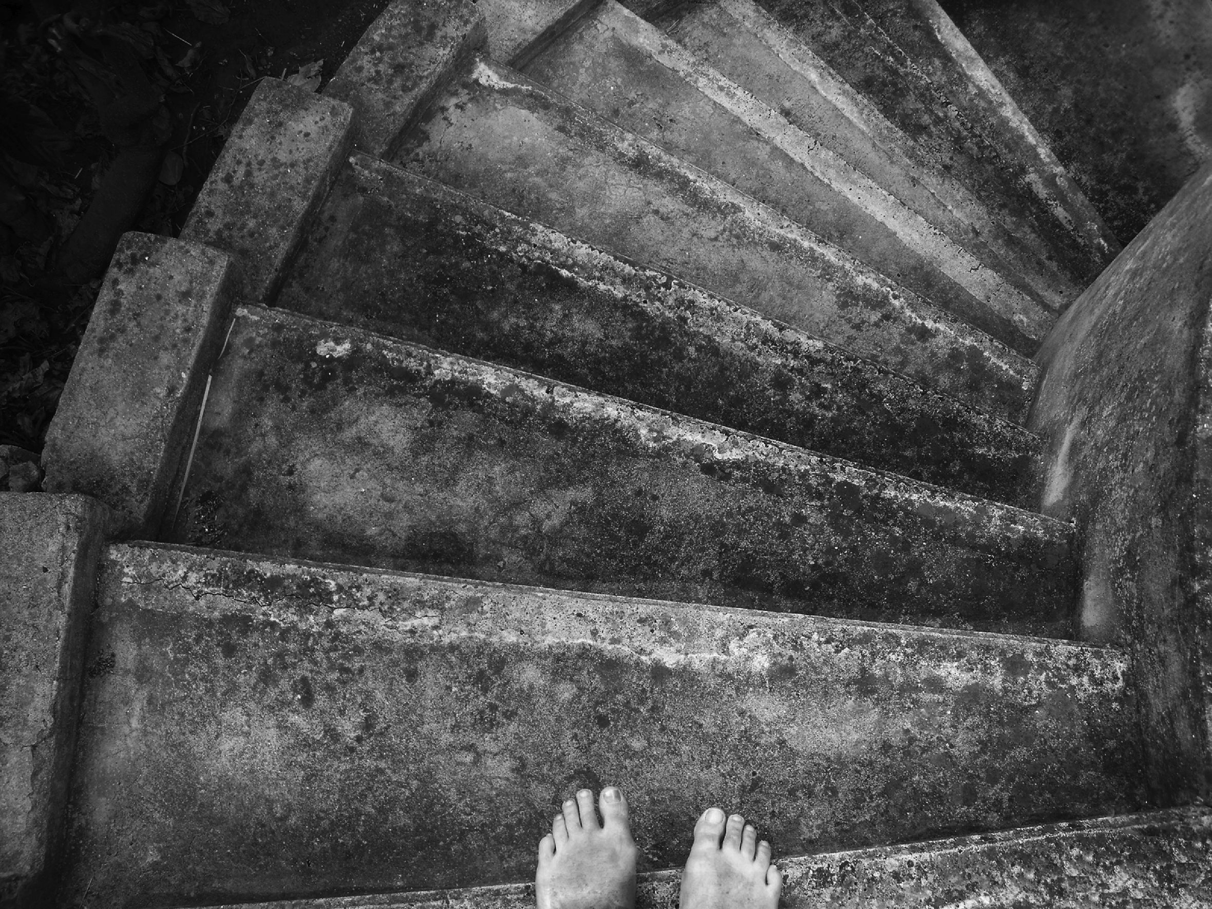 Spiral cement stairway shot from above with bare feet protruding over the top step.