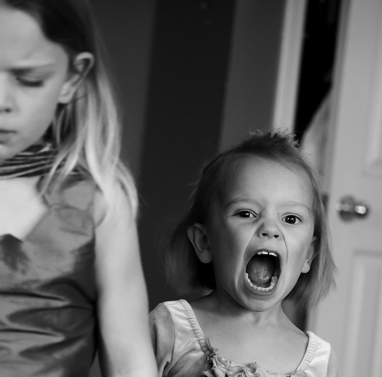 A young girl screaming near an older girl who has her eyes closed and looks frustrated.