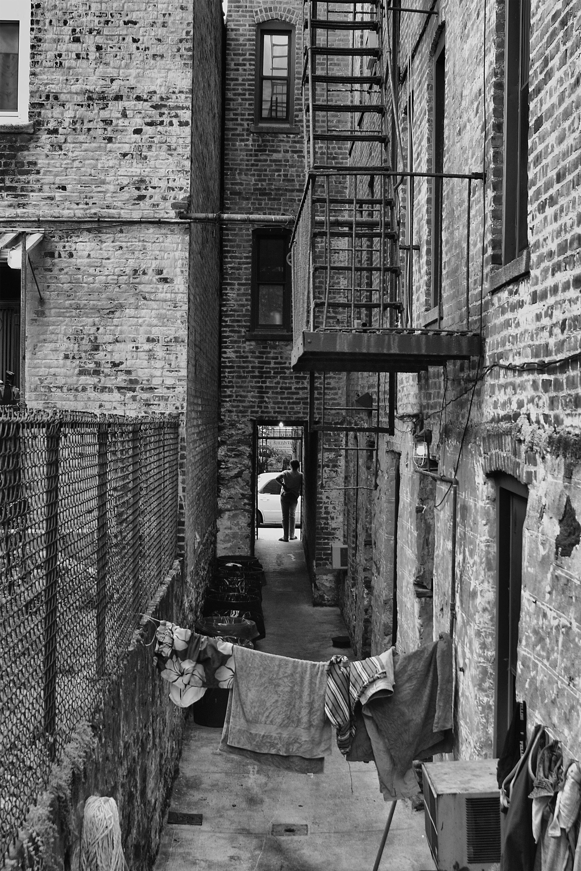 The alleyway between adjacent brick buildings in the city. Clothes and towels hang on a clothesline between the buildings.