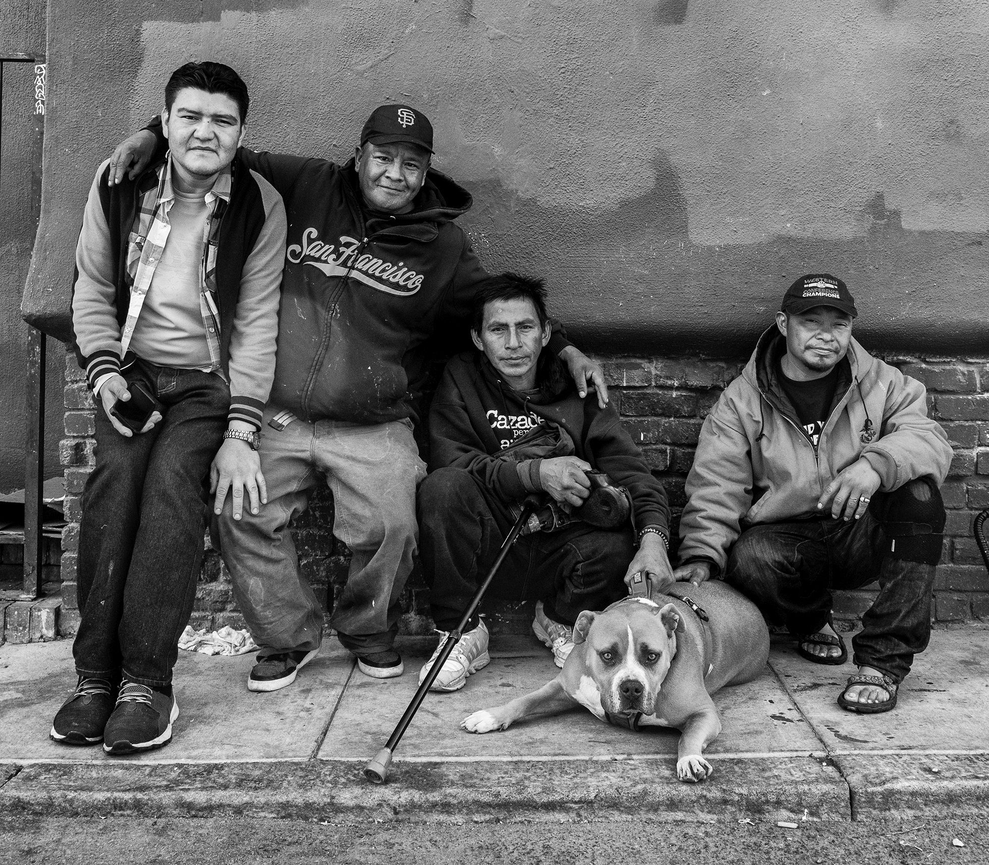 Manuel, Franco, Edwin, Jorge, and Cabezón, Edwin’s pit-bull mix, gather on a sidewalk in San Francisco in October 2019. Franco smiles and he has his arms over the shoulders of Manuel and Edwin, and both Edwin and Jorge have a hand on Cabezón’s back.
