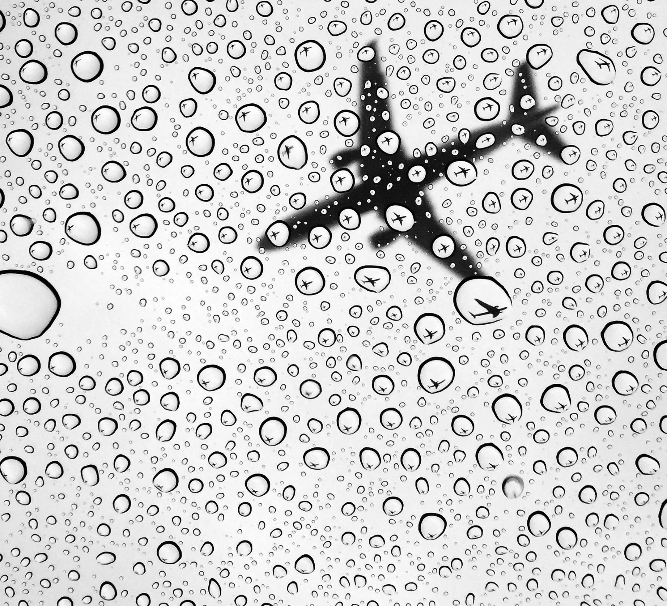 A passenger plane overhead at the Detroit Metro Airport seen from beneath clear glass or plastic covered with water droplets. Inside some of the droplets is the complete reflection of the plane.