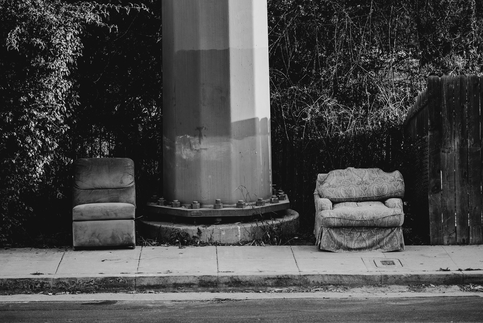 Two couch chairs on the sidewalk face the street on either side of an electric pole in the Silver Lake neighborhood of Los Angeles. The two chairs seem both out of place and settled, as if someone had placed them there with purpose.
