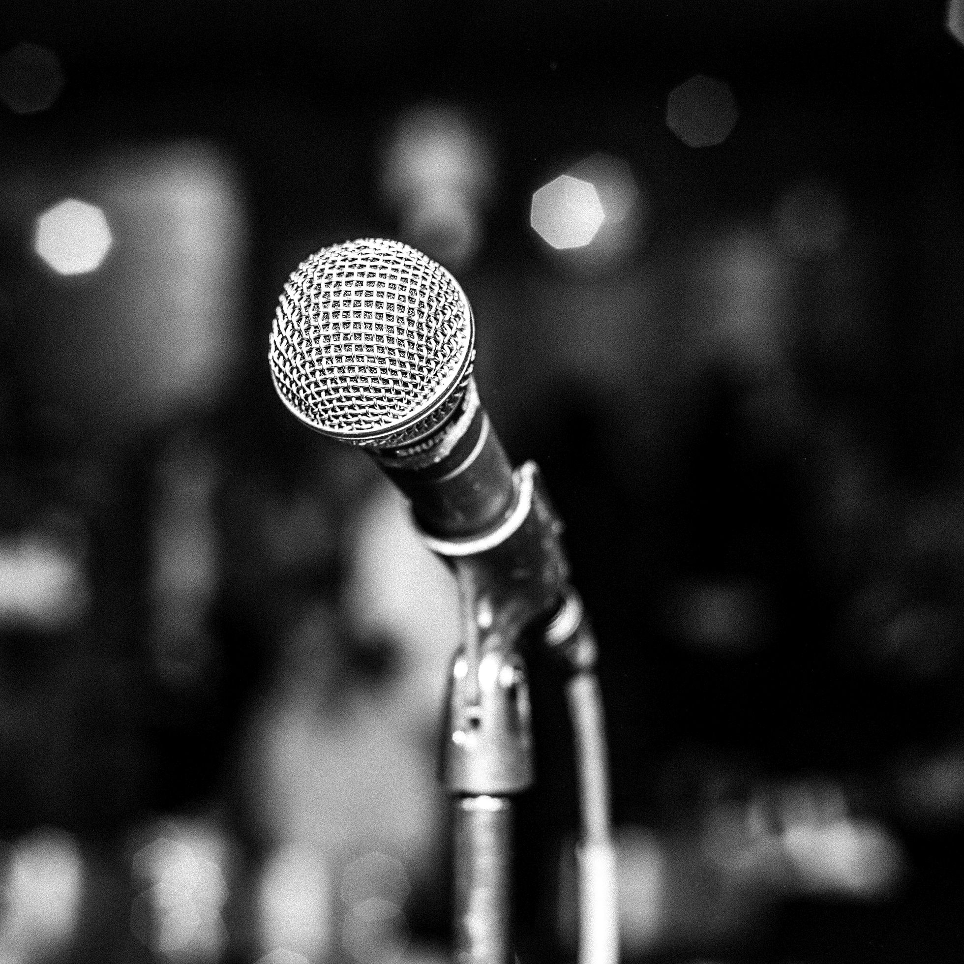 Close-up of a microphone on a stand from the stage side looking out into the room with the people and room blurred in the background.