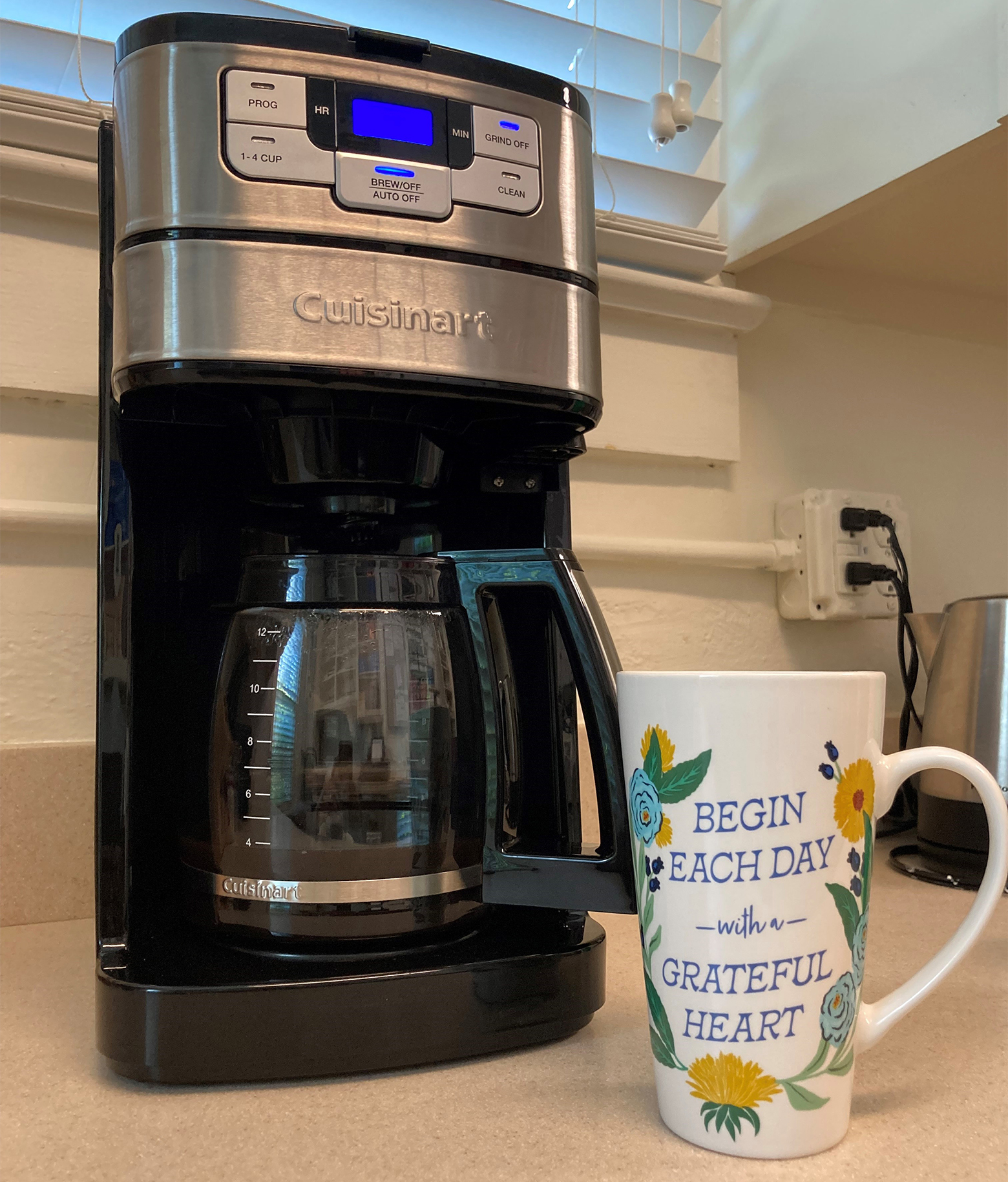 Coffee mug that reads Begin Each Day with a Grateful Heart on a counter next to a Cuisinart drip coffee maker.
