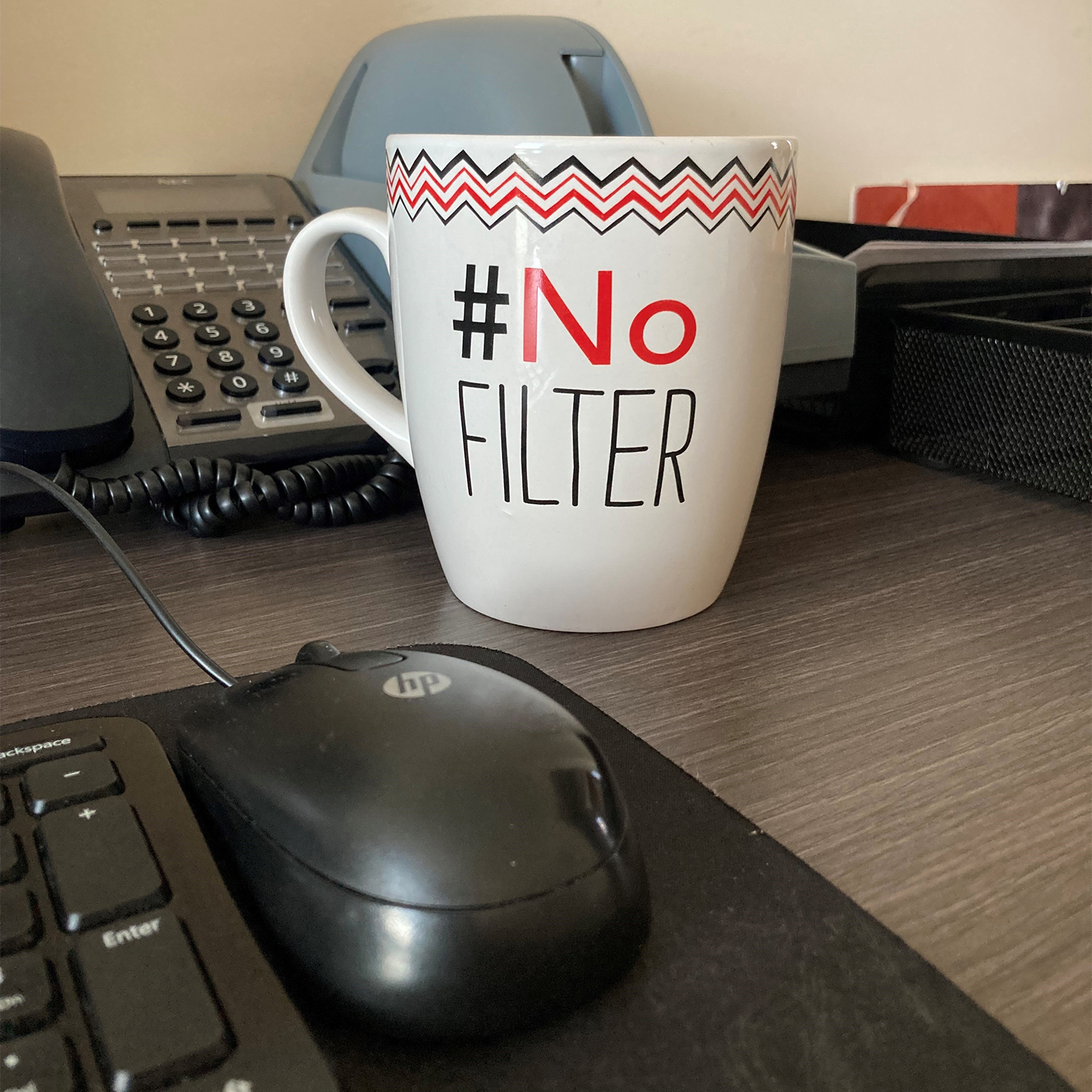 Coffee mug that reads # No Filter on an office desk.