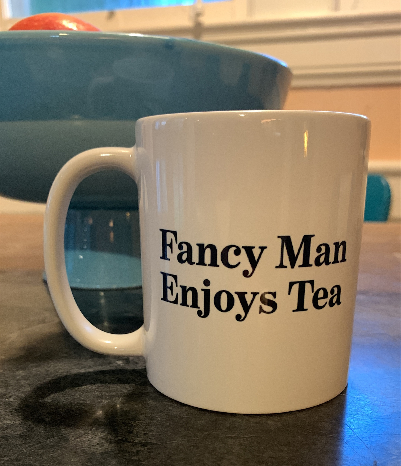 Coffee mug  that reads Fancy Man Enjoys Tea is set on a kitchen counter.