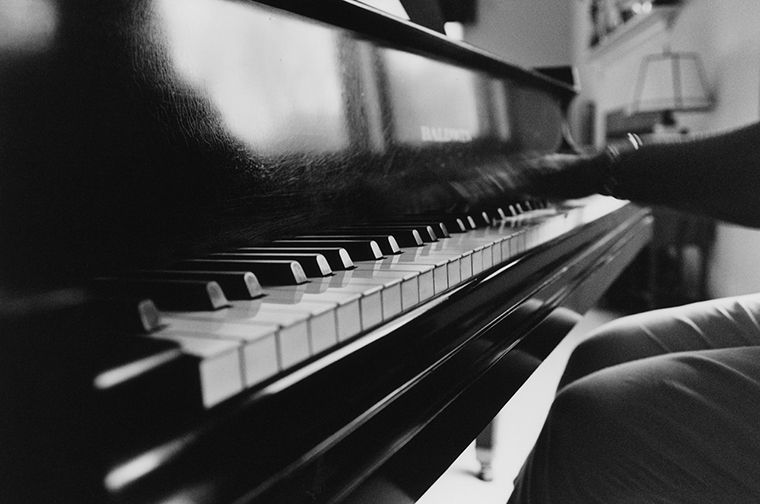Close-up of a piano and the hands and knees of the person playing it.