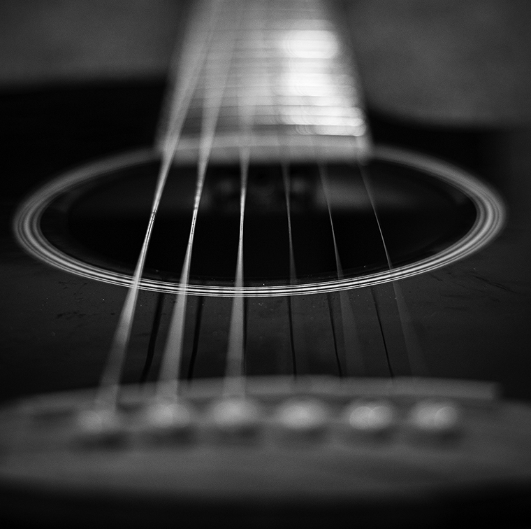 Blurry close-up of the neck and sound hole of a guitar.