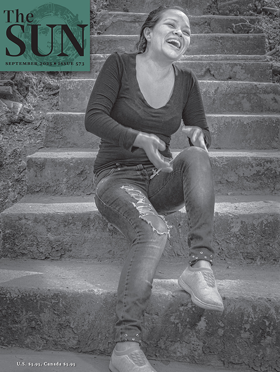 September 2023 cover of The Sun. Thom Goertel took this month’s cover photo, of Teresa Cruz Morales, near Cuernavaca, Mexico, in early 2020. Teresa smiles and laughs while sitting on a concrete stairway.