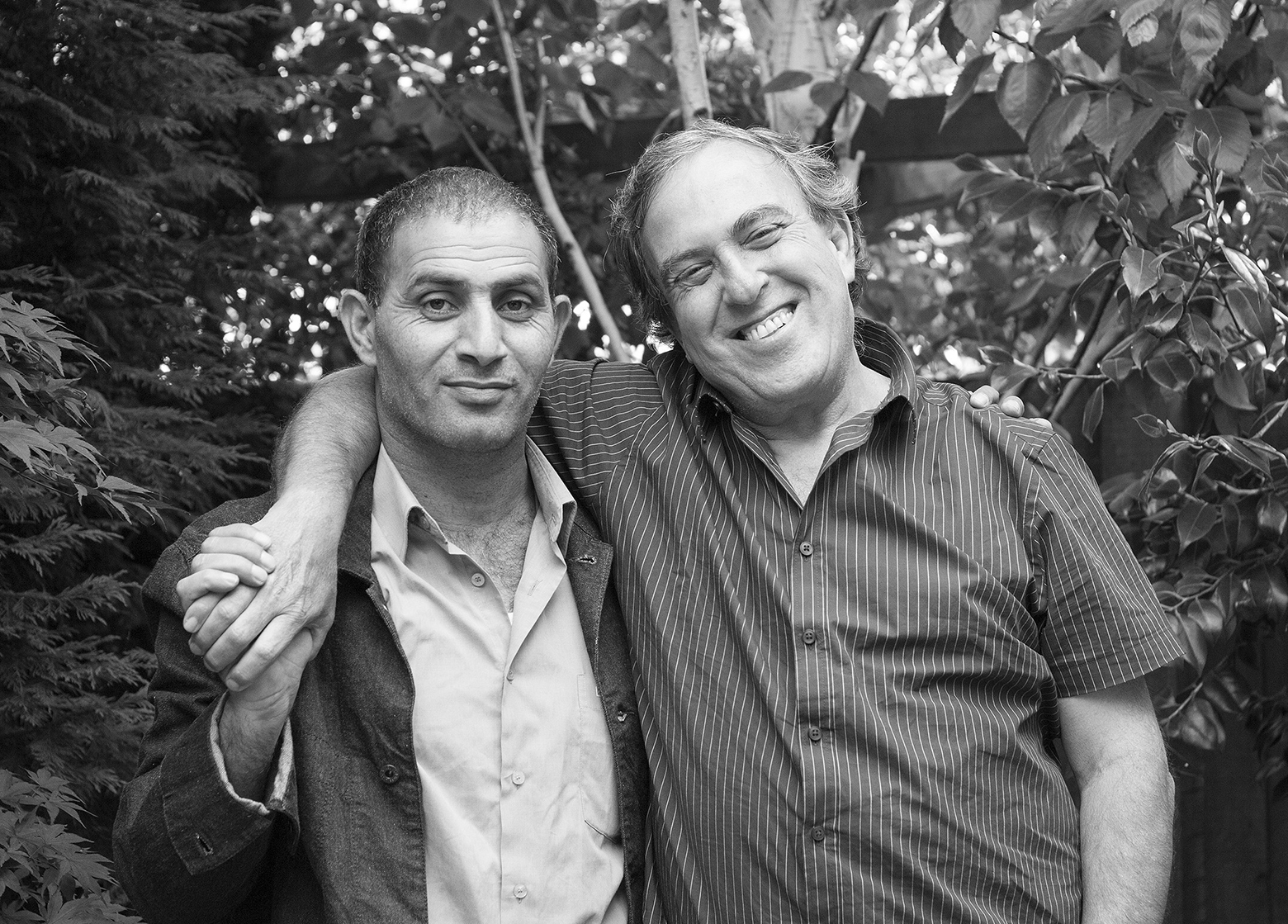 Bassam Aramin and Rami Elhanan in London on June 2013. Both men smile as they stand with their arm over the other’s shoulders. Aramin clasps Elhanan’s hand.
