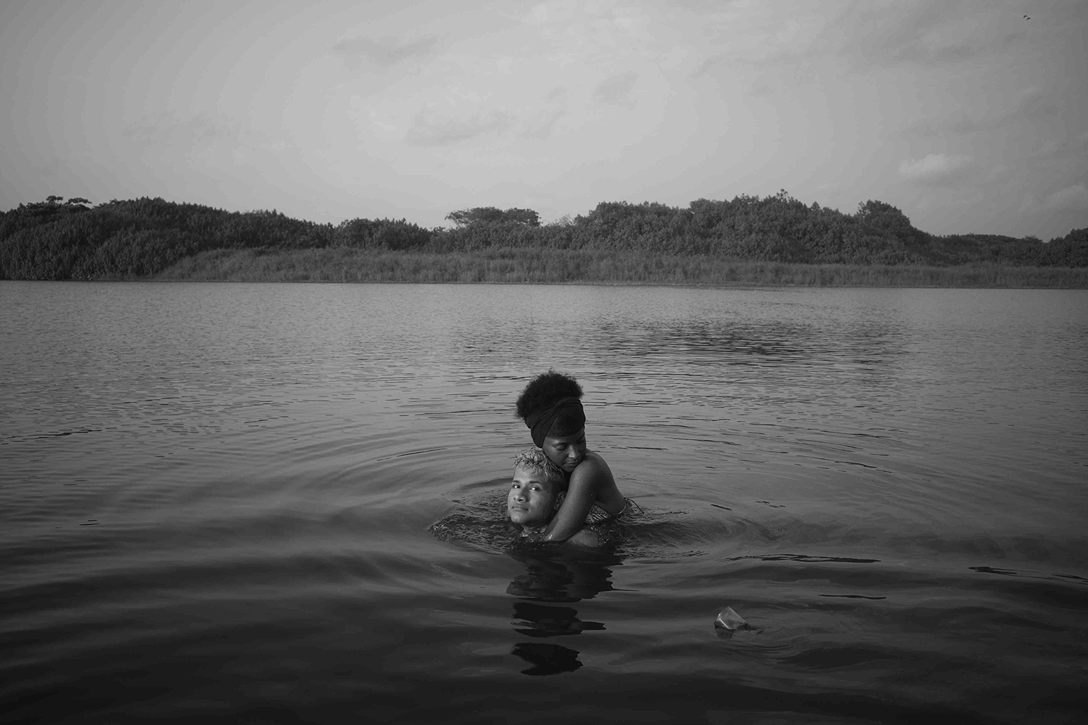 Erick and Maritza swim in a lagoon outside of Collantes, Oaxaca. Erick is looking at the camera while Maritza has her eyes closed as she holds Erick from behind with her arms around his neck.
