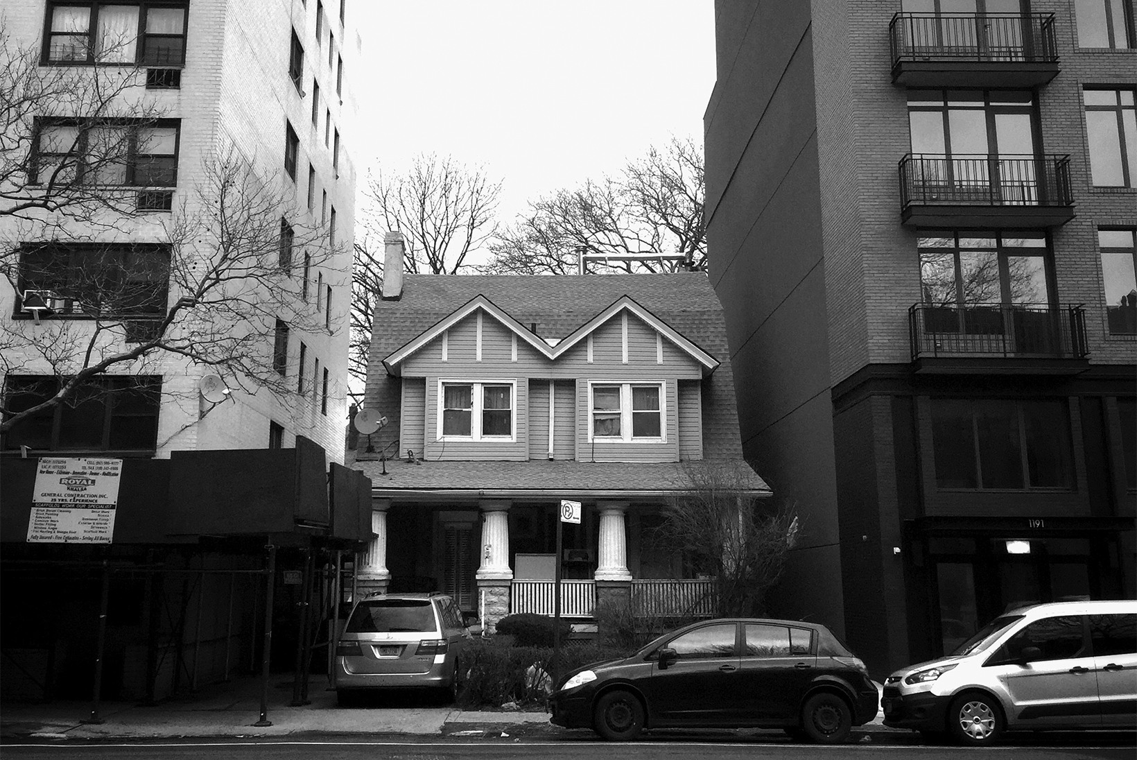 A small two-story house is sandwiched between two high-rise apartment buildings.