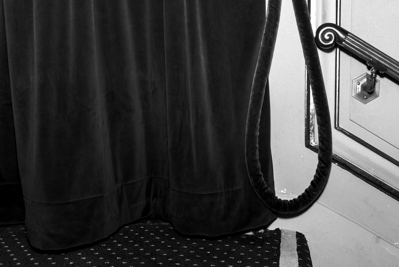 Carpeted steps in a theater lead to a heavy velvet curtain and velvet rope hanging against a wall.