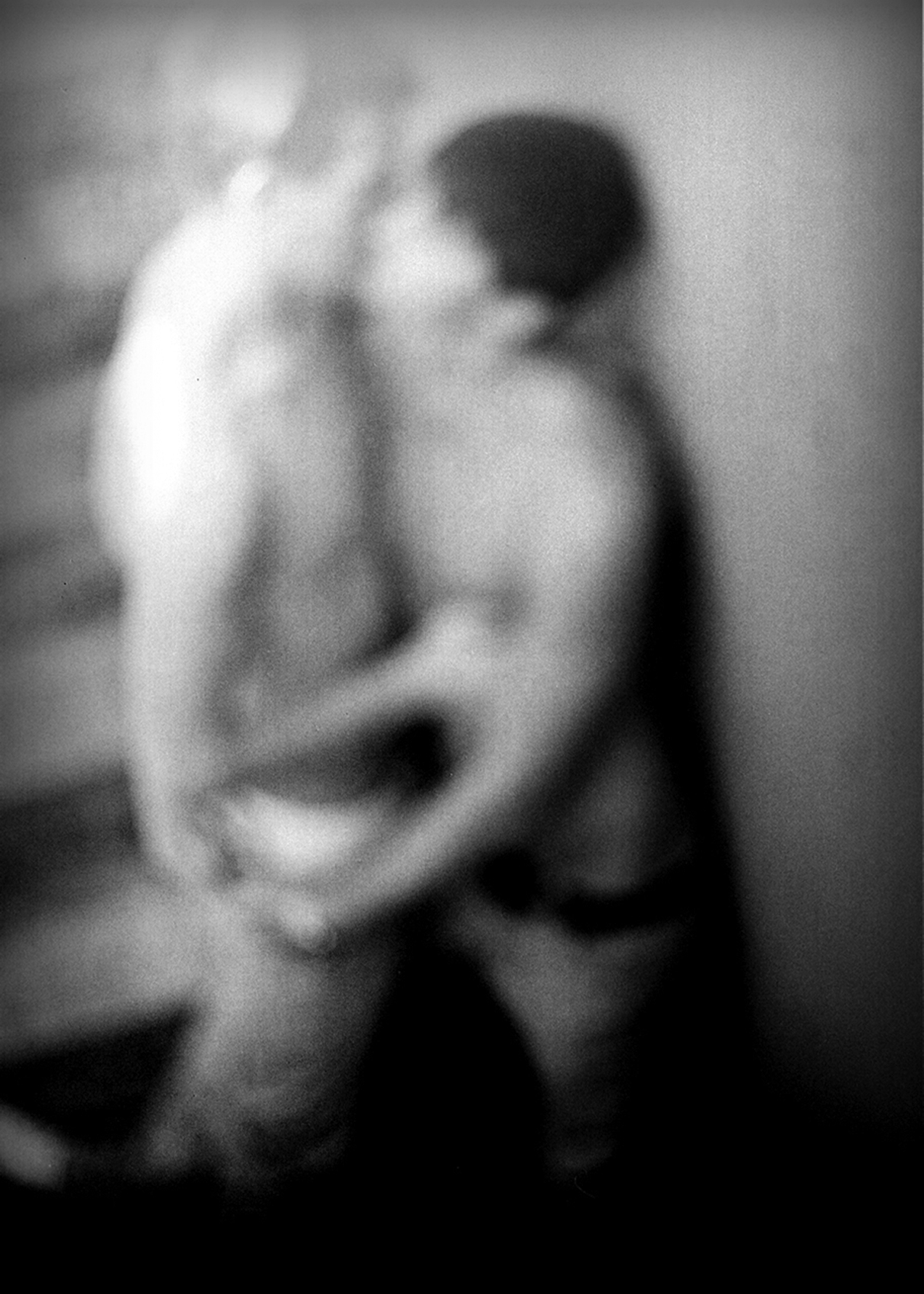Blurry photo of two shirtless men standing in a stairway and kissing.