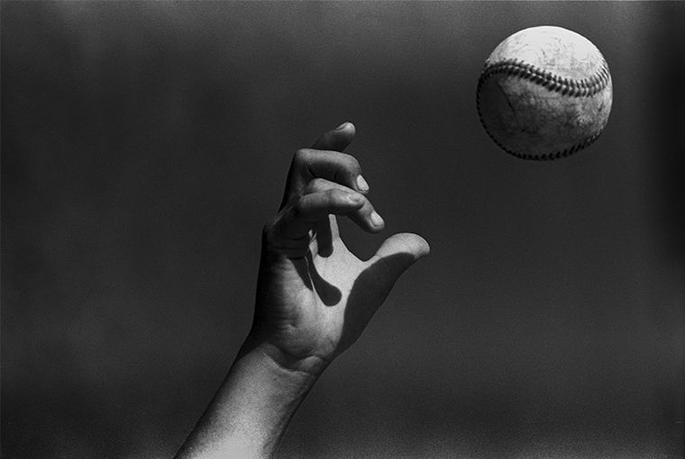 Close-up of a hand in the air and a just-released baseball. The fingers are positioned to have just thrown a curveball.
