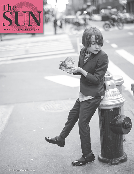 May 2024 cover of The Sun. A young boy wearing a three-piece suit and his sister’s tap shoes leans against a fire hydrant while eating a slice in New York City after having seen a musical on Broadway.