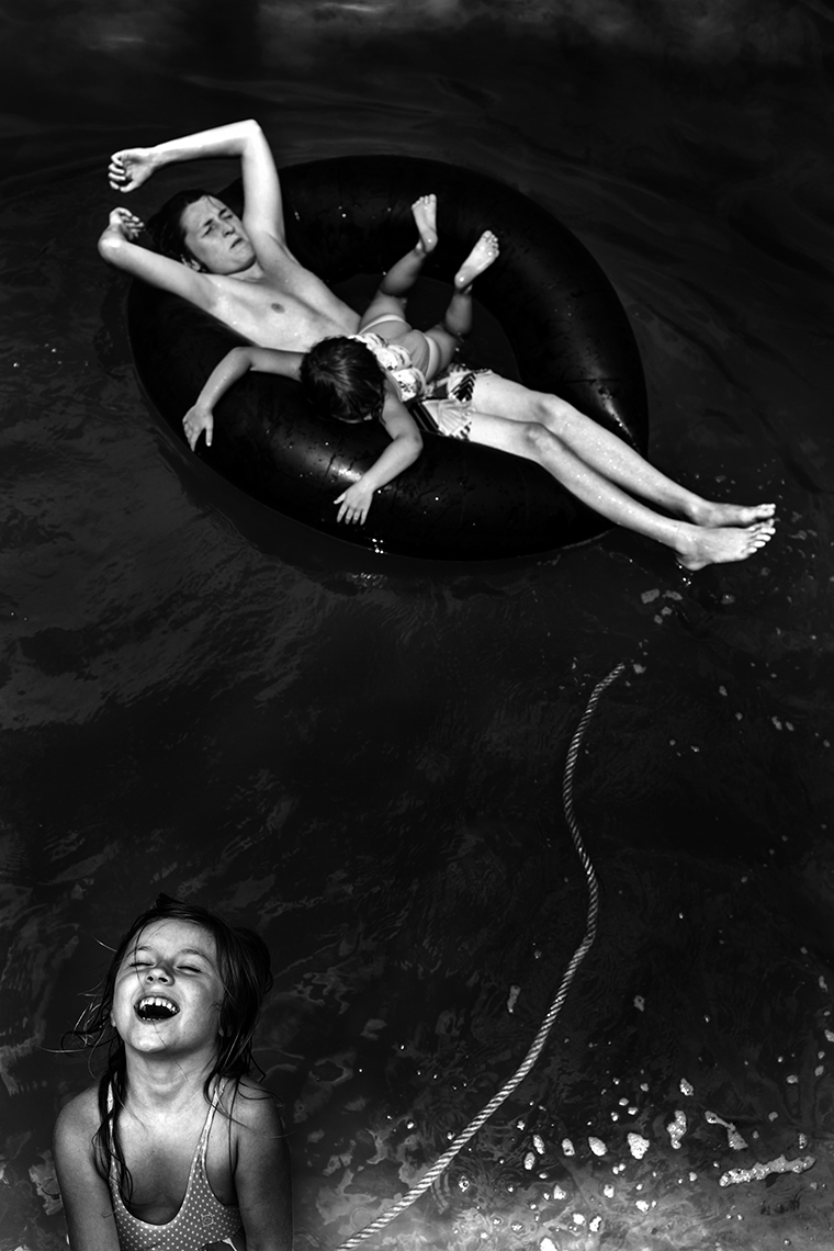 A young boy with his eyes closed and hands behind his head is stretched across an inner tube floating on the water and tethered to a rope his laughing younger sister has hold of. Another sister is stretched on top of him face down and crosswise.