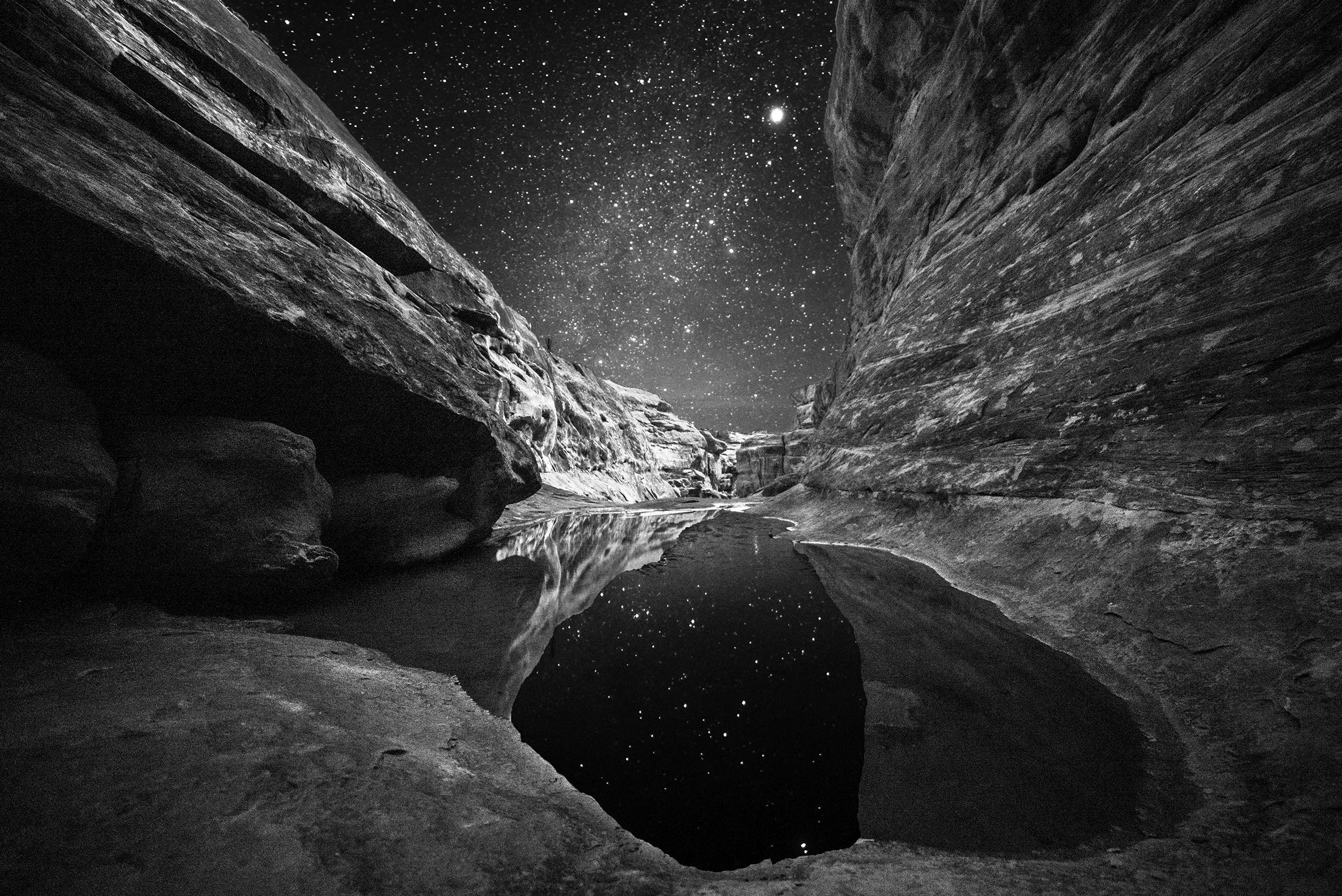 The photo titled “Nocturnal Images: Redman Pool” was taken of a pool at the bottom of a canyon with steep, close-in walls on a starry night. The reflections of the stars are visible in the water.